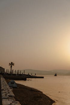 Peaceful beach scene at sunset with silhouetted boat and palm tree, perfect for serene wallpapers.