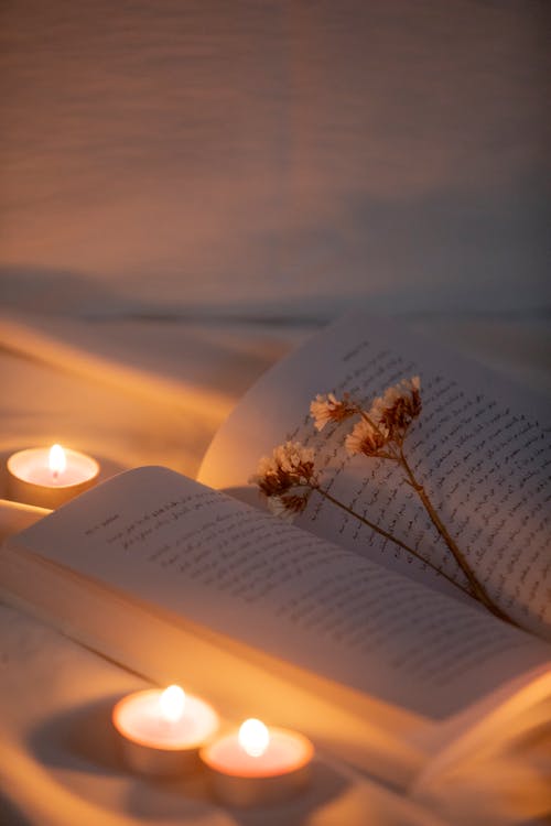 An Open Book with Dried Flowers on a White Blanket Surrounded with Lighted Candles
