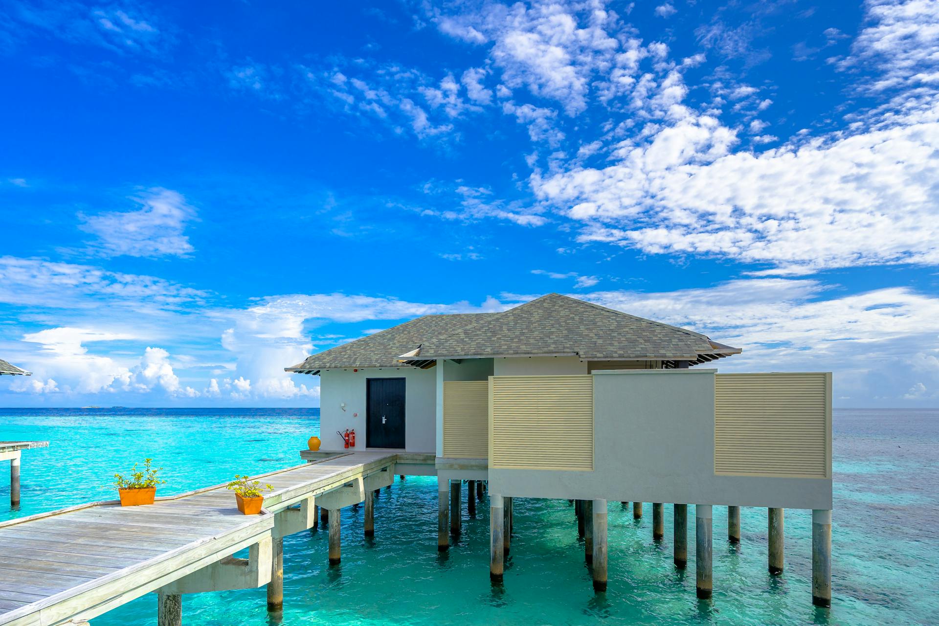 Stunning overwater villa on turquoise ocean with a wooden dock and clear blue sky, perfect for tropical getaways.