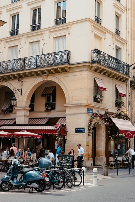 A picturesque Parisian street scene with a busy café, tourists, and parked scooters.