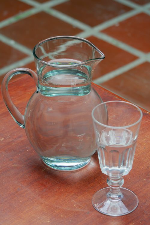 Free A clear glass pitcher with matching drinking glass on a wooden table, reflecting simplicity and elegance. Stock Photo