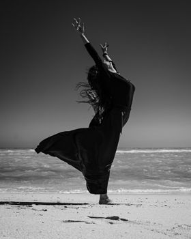 A woman gracefully poses on a windy beach, captured in black and white.