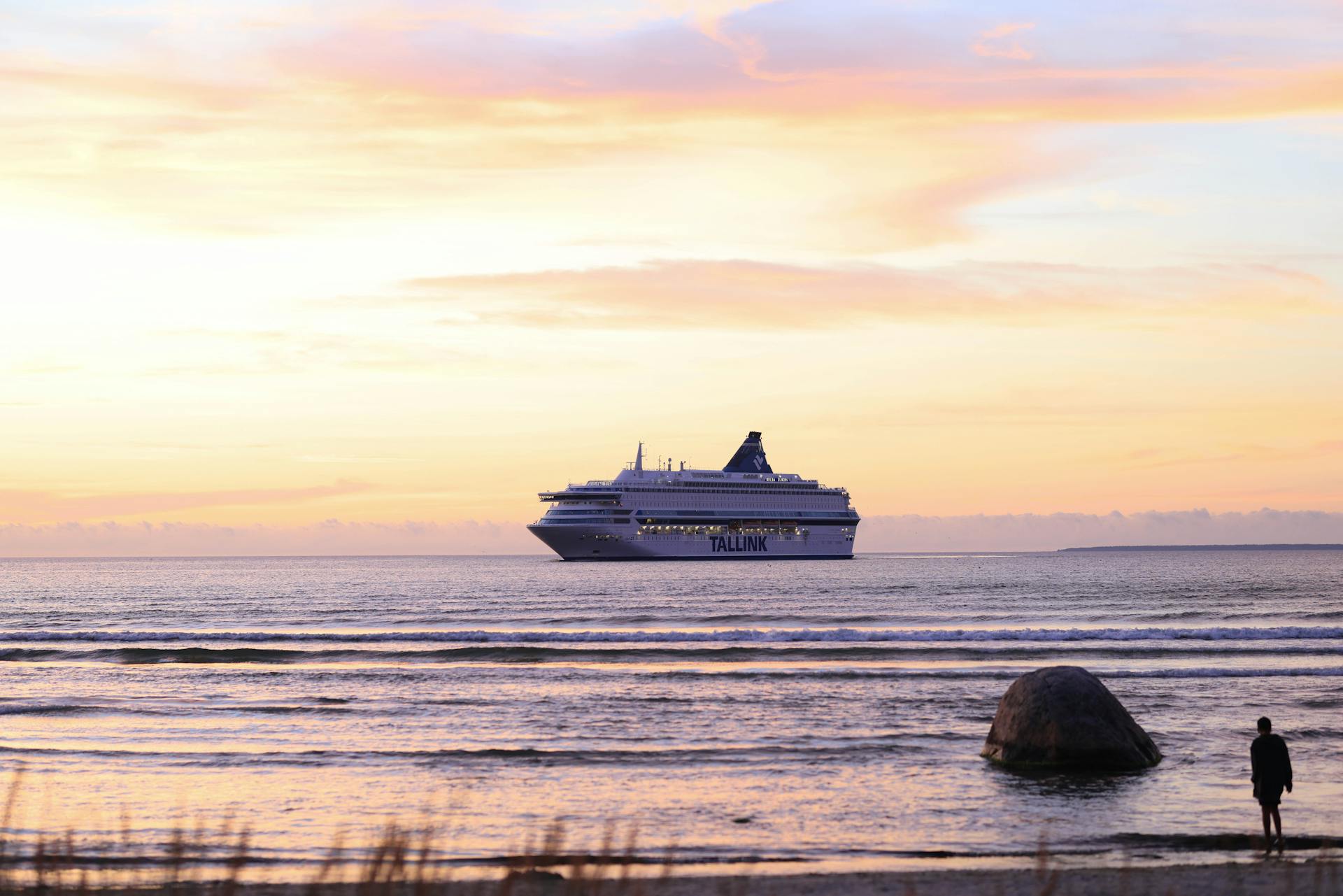 A cruise ship sails on tranquil waters during a stunning sunset, creating a serene travel scene.