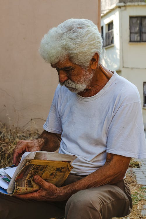 Man in T-shirt Sitting and Reading Newspaper