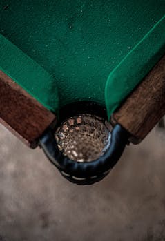 Detailed view of a billiard table's corner drop pocket with green baize and wooden edge.