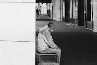 一张黑白照片中，一位老人坐在城市的长凳上，透露出孤独感
