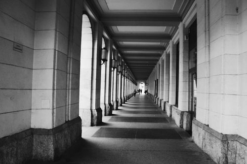 Free Monochrome image of a symmetrical hallway with columns and shadows, reflecting urban architecture. Stock Photo