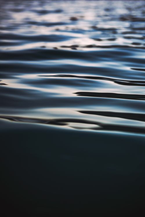 Free A close-up of rippling water reflecting light, creating a serene and calming effect. Stock Photo