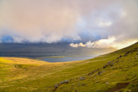 Tranquil view of Eysturoy's green hills, cloud-covered sky, and lake on a peaceful day.