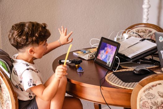 Young boy using tablet for online learning at home, surrounded by electronic gadgets.