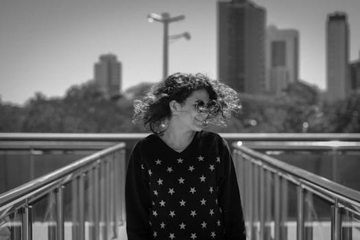 一位戴着墨镜的女子在城市的桥上微笑，为城市景观增添了活力