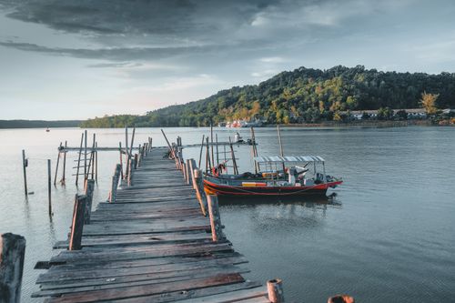 Free A picturesque wooden pier leading to a boat on a tranquil lake surrounded by lush hills. Stock Photo