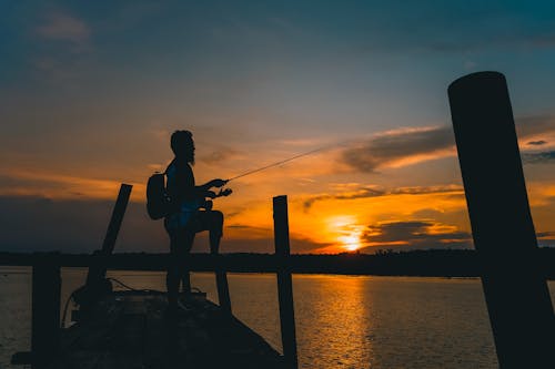 Man Standing on Wooden Dock during Sunset