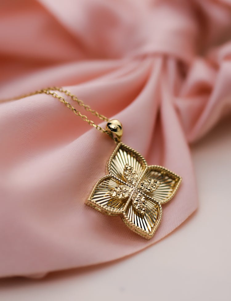 Gold Necklace With Flower Design Pendant On A Pink Surface