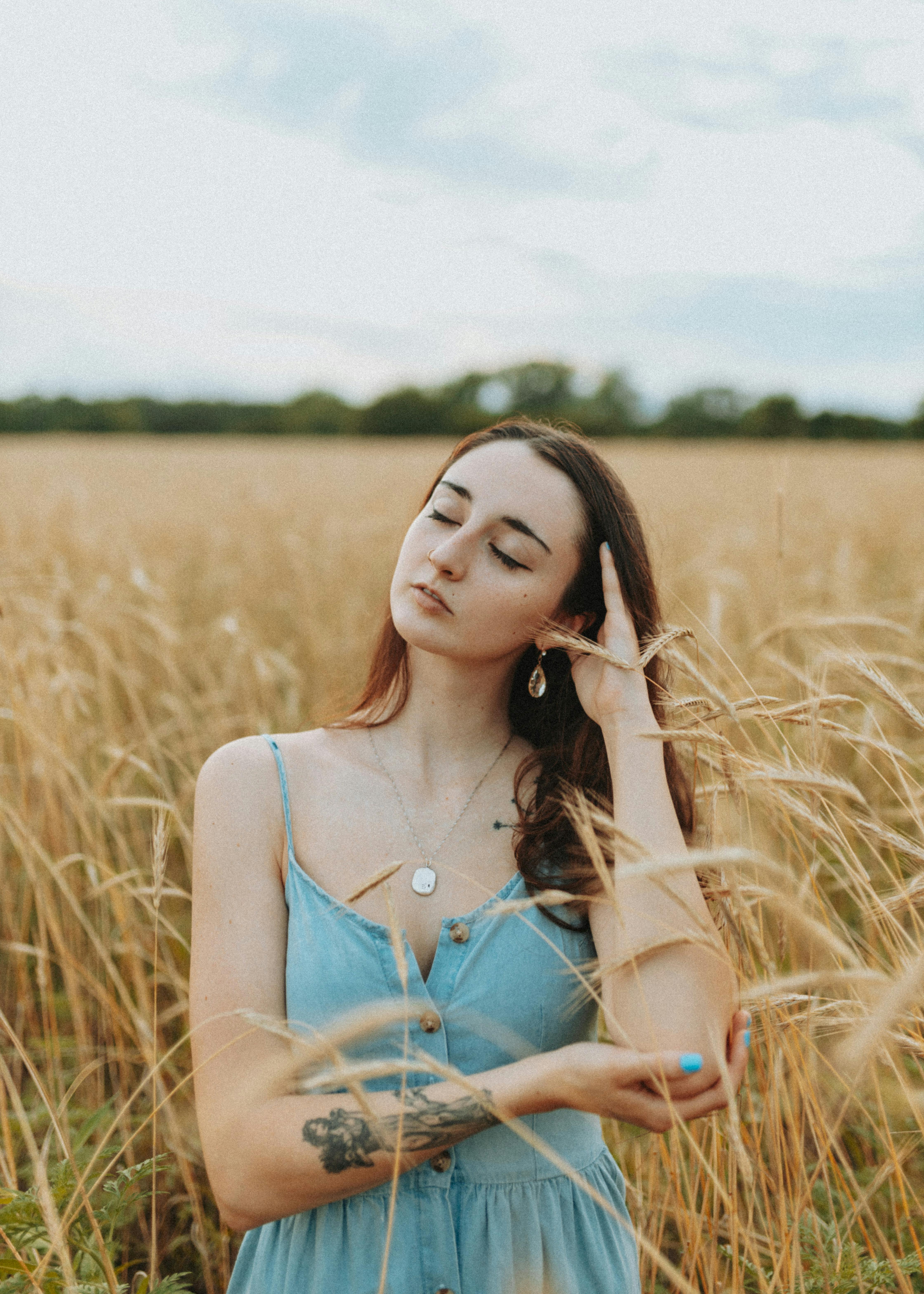 Woman in summer dress posing thoughtfully in a wheat field during daytime, showcasing natural beauty and tranquility.
