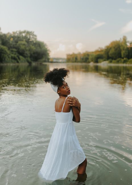 A woman in a white dress standing in a tranquil river during sunset.