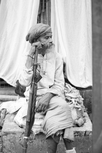 A senior man sits outdoors with a stick, conveying wisdom and experience.