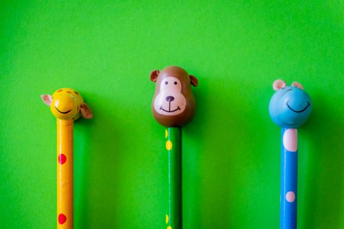 Free Three animal-themed pencils with colorful tops against a vibrant green background. Stock Photo