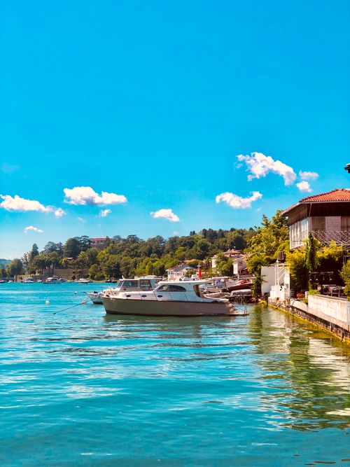 Free Tranquil lakeside with docked boats under a bright blue sky and lush greenery. Stock Photo