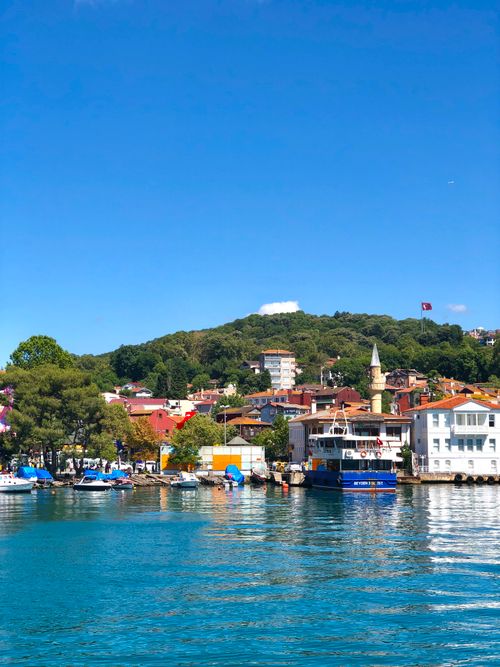 Free Charming waterfront village with boats, colorful houses, and lush green hills under a clear blue sky. Stock Photo