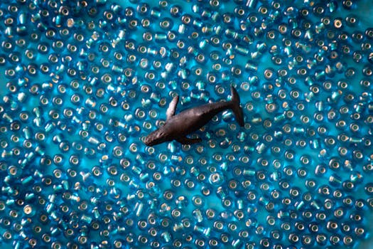 一只微型鲸鱼玩具漂浮在蓝色珠子的海洋上，捕捉着运动和色彩