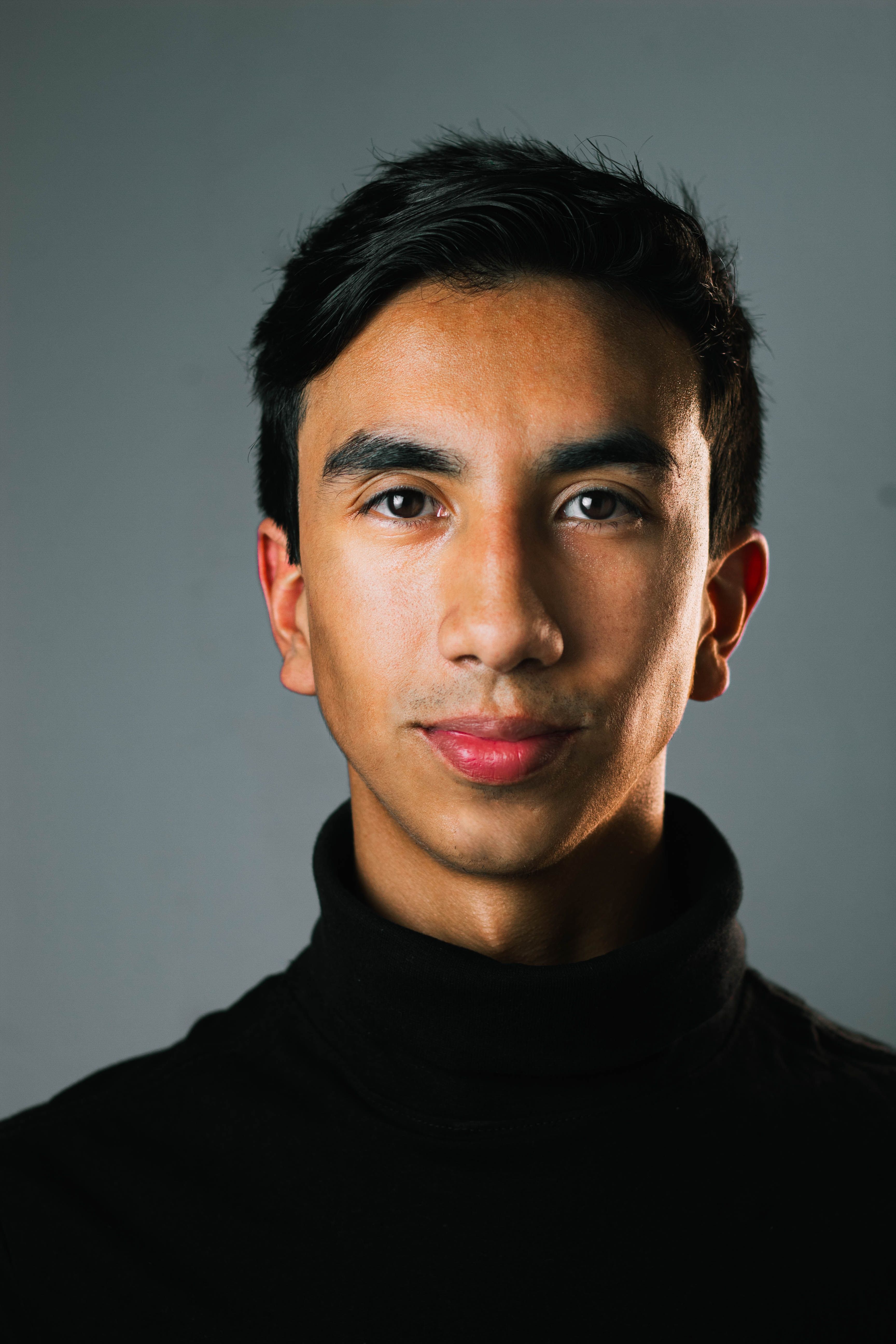 Close-up portrait of a young man in a black turtleneck, studio setting.
