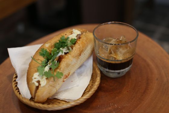 Banh mi baguette with pork, mayo and cilantro in a small basket beside iced coffee