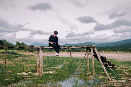Free A lone man reading on an old wooden bridge amidst a lush landscape. Stock Photo