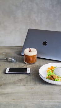 A contemporary workspace featuring a laptop, iced coffee, and a healthy lunch plate.