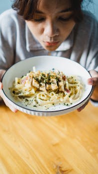A person holding and savoring a creamy fettuccine pasta with herbs and grilled chicken.
