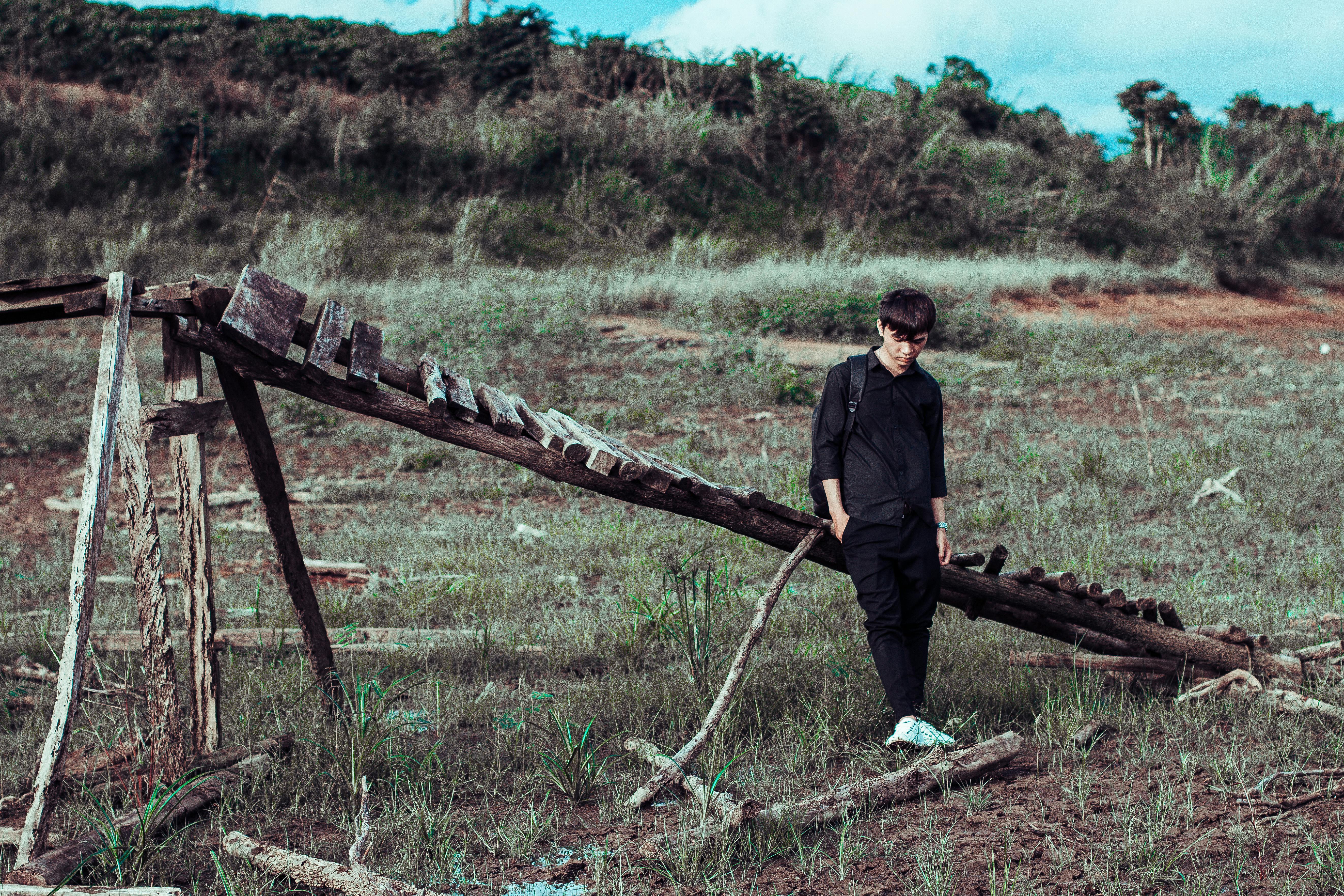 man leaning on wooden bridge on grass field