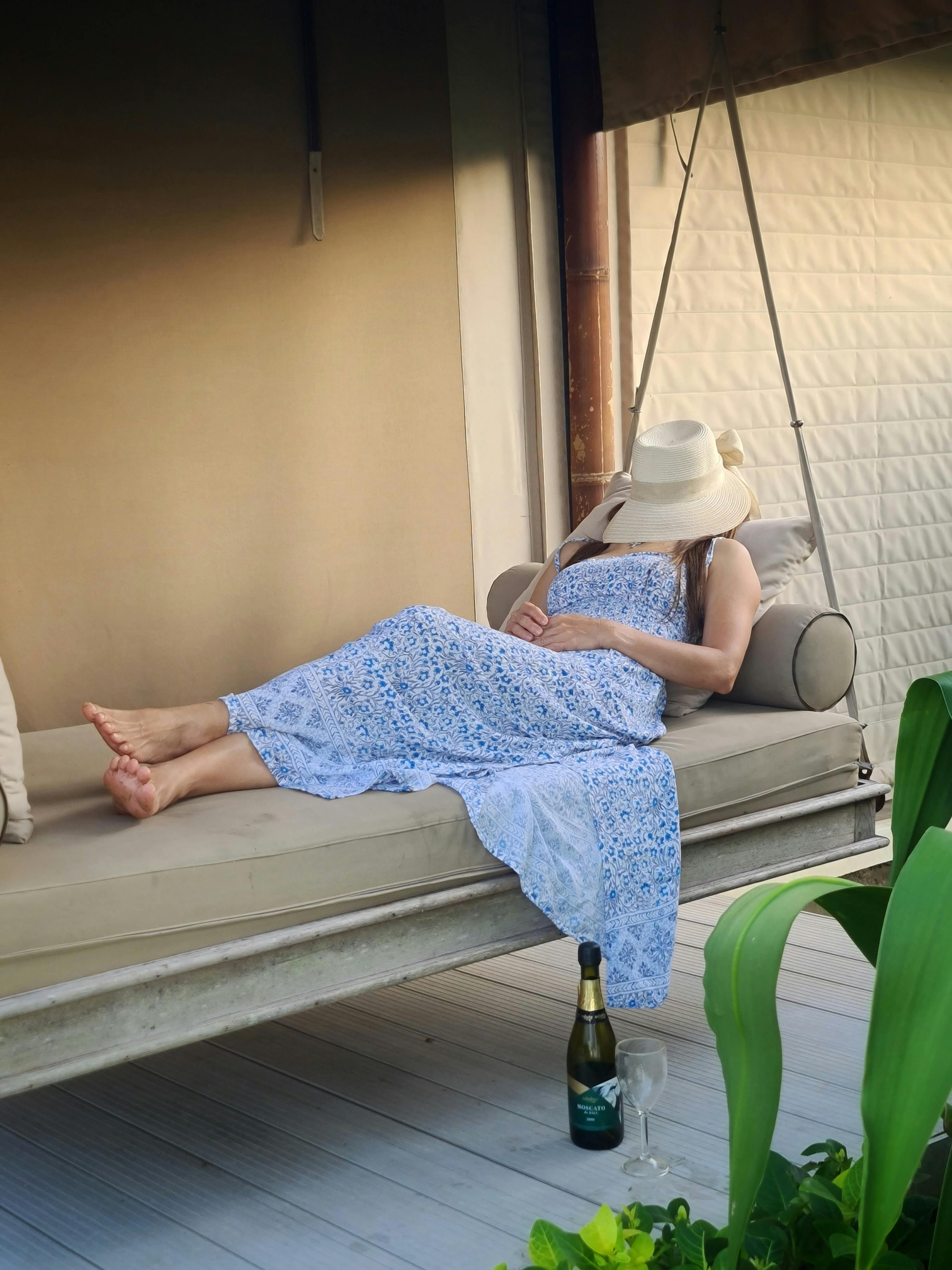 Free A woman in a blue dress relaxes on a swinging couch with wine in Kuta, Indonesia. Stock Photo