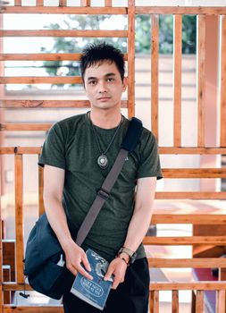 一名年轻男子在户外休闲地拿着书和书包，显得若有所思