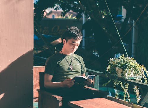 Человек читает книгу возле зеленых деревянных перил