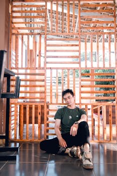 一个男人穿着休闲服和运动鞋，若有所思地坐在室内，靠着一个木制隔板