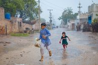 A joyful scene of children running through rain-soaked streets in Sargodha.