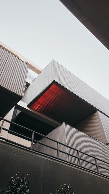Contemporary building facade with corrugated panels and red ceiling detail.