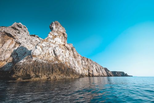 Free Majestic rocky cliffs along a serene ocean coast under a vibrant blue sky, perfect for nature enthusiasts. Stock Photo