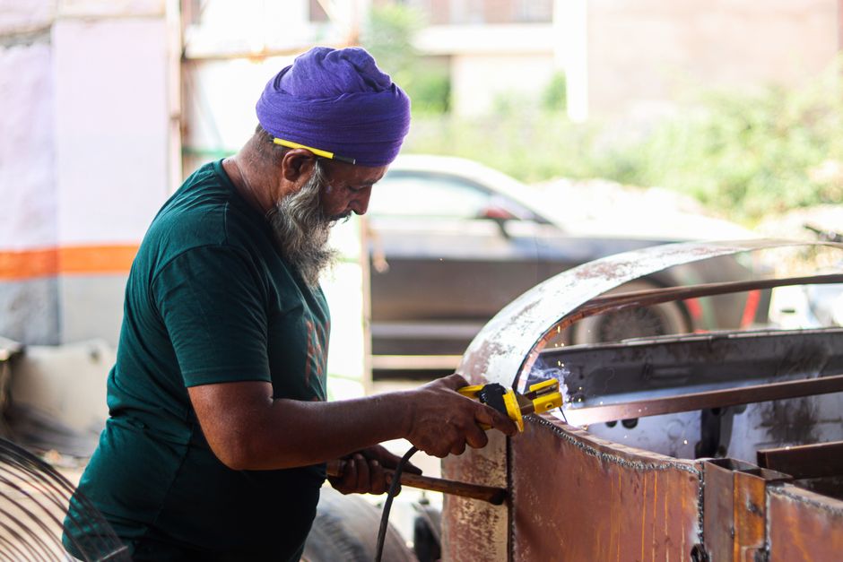 Elderly man with turban welding metal in a workshop, showcasing skilled craftsmanship.