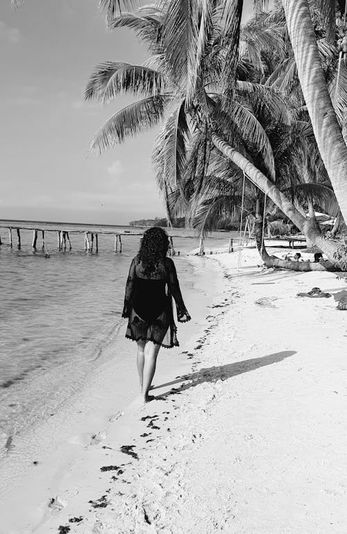 Grayscale Photo of Woman Walking on Shore