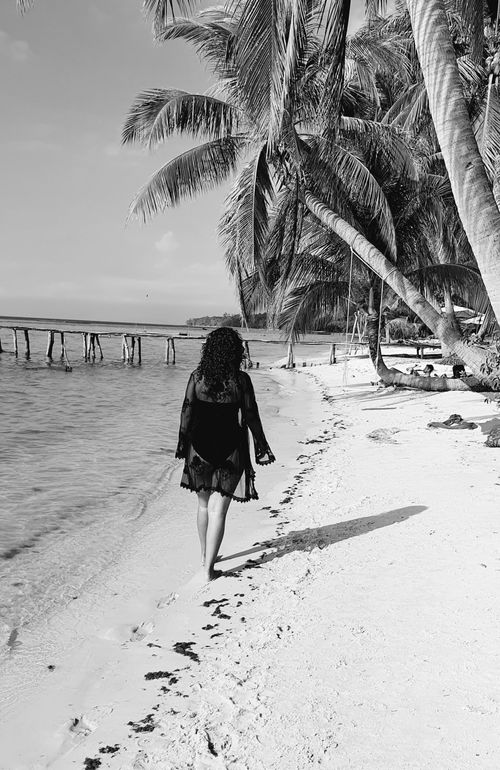 Free Woman walking along the palm-lined shore in Phú Quốc, Vietnam. Black and white elegance. Stock Photo