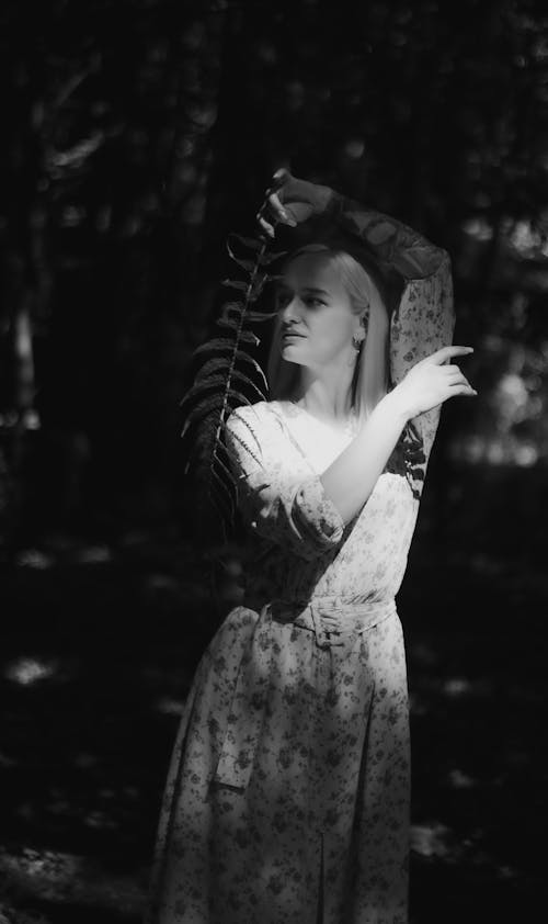 Grayscale Photo of a Woman in Floral Dress Holding a Fern Leaf 