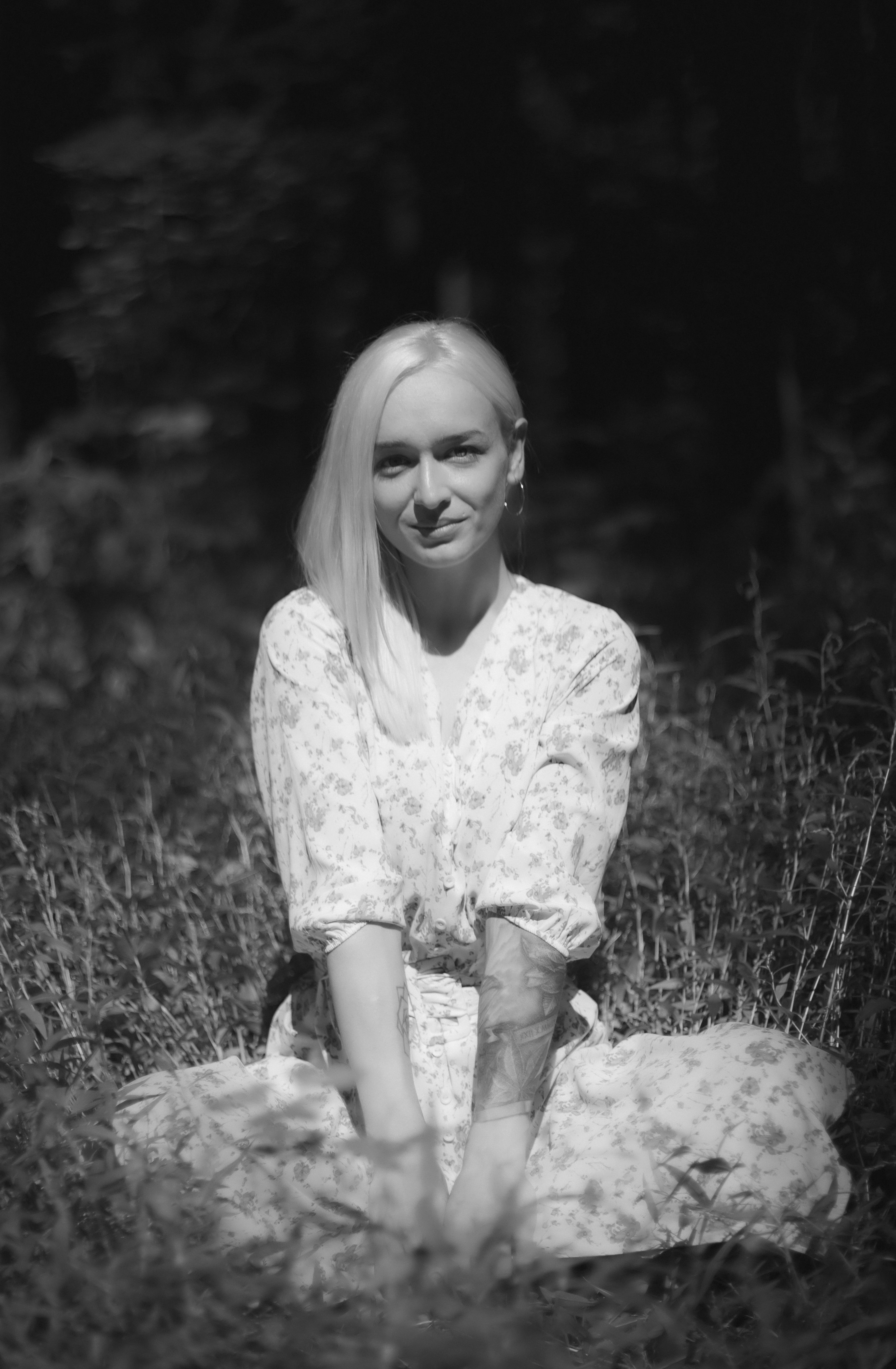 A serene monochrome portrait of a woman sitting amidst nature, bathed in soft light.