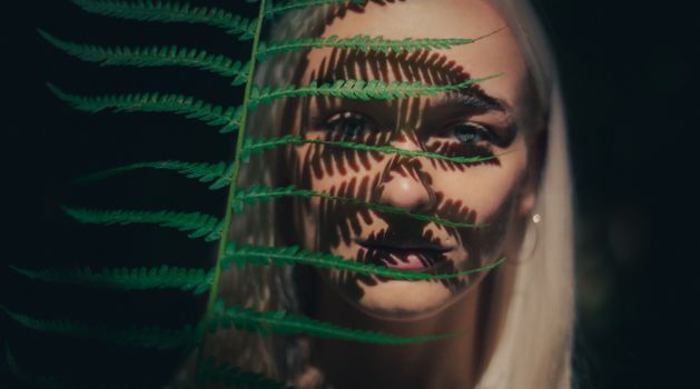 Close-up portrait of a woman with fern leaf shadows on her face, creating an artistic and mysterious effect.