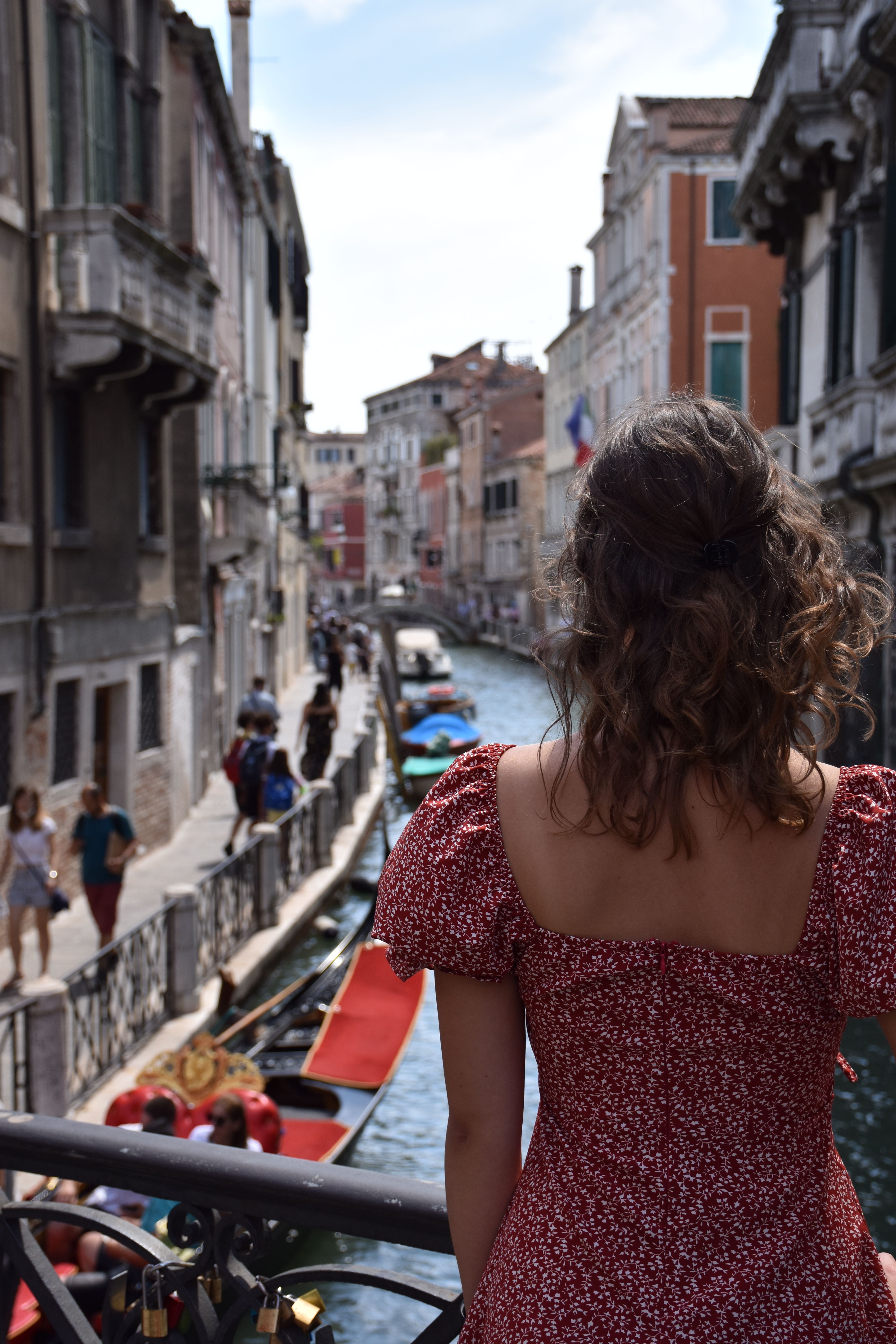 A woman in a floral dress stands on a bridge overlooking a canal in Venice, Italy, capturing urban and scenic beauty.