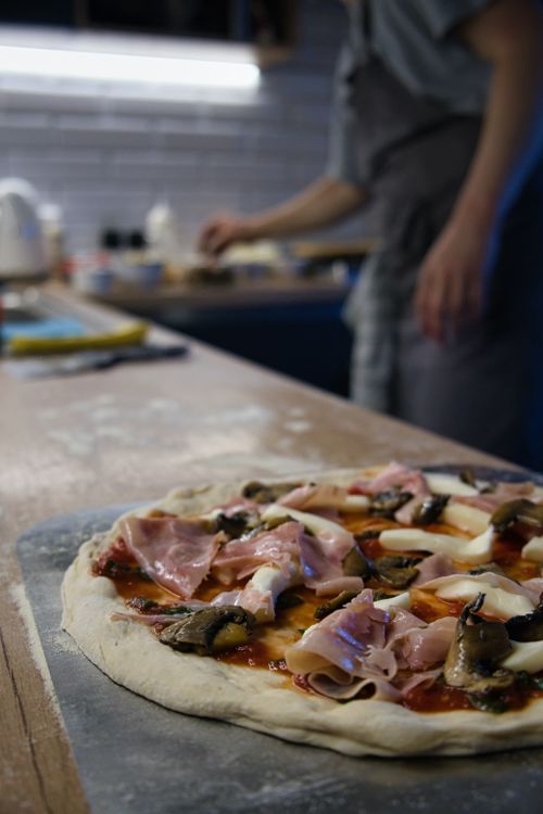 Free Close-up of a delicious homemade pizza with prosciutto, cheese, and mushrooms on a kitchen counter. Stock Photo
