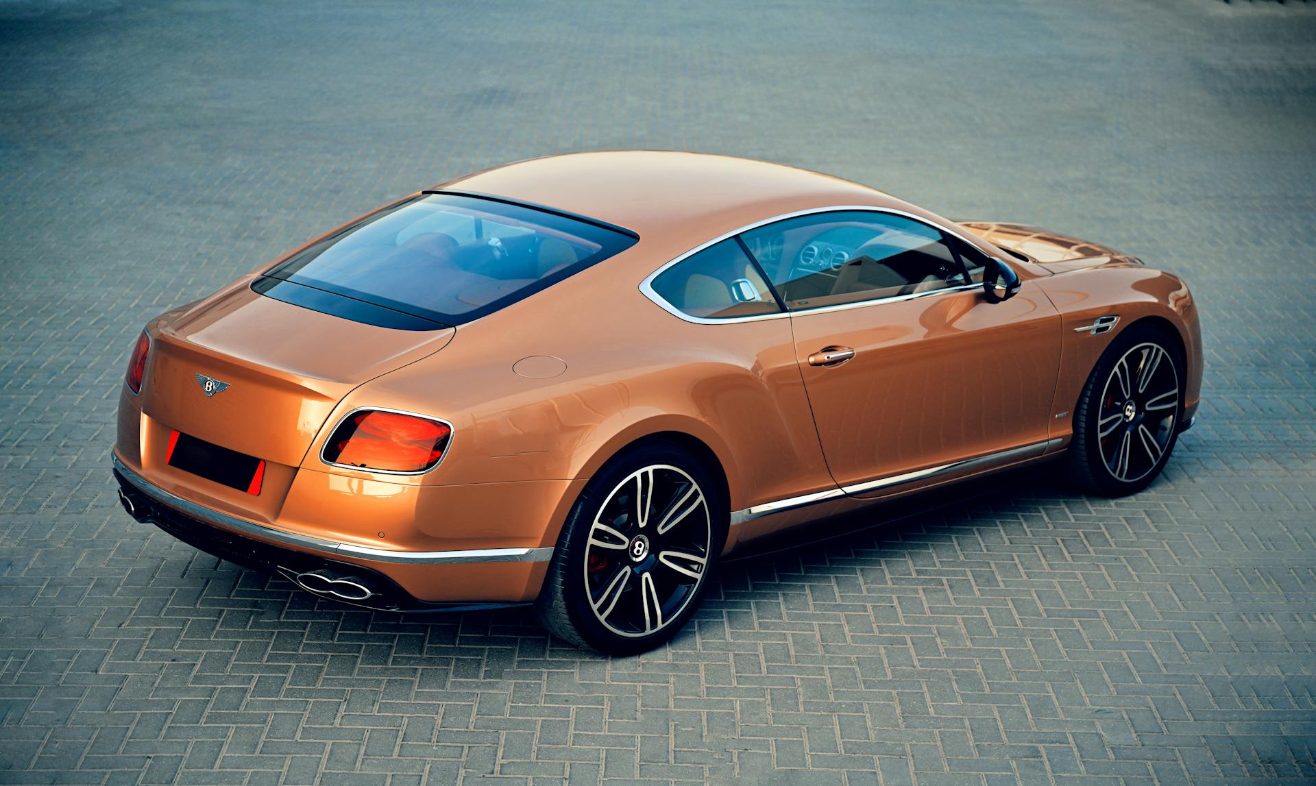 Rear view of an elegant orange Bentley car parked outdoors showcasing luxury and style.