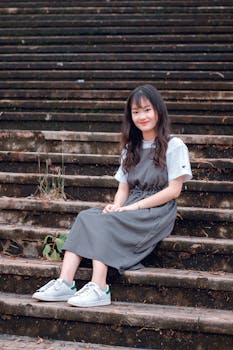 一位年轻女子身着便装，坐在户外楼梯上热情地微笑着