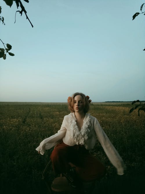 Woman in White Long Sleeve Sitting on Green Grass Field