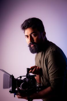 A videographer with a beard holding a camera in a studio setting.
